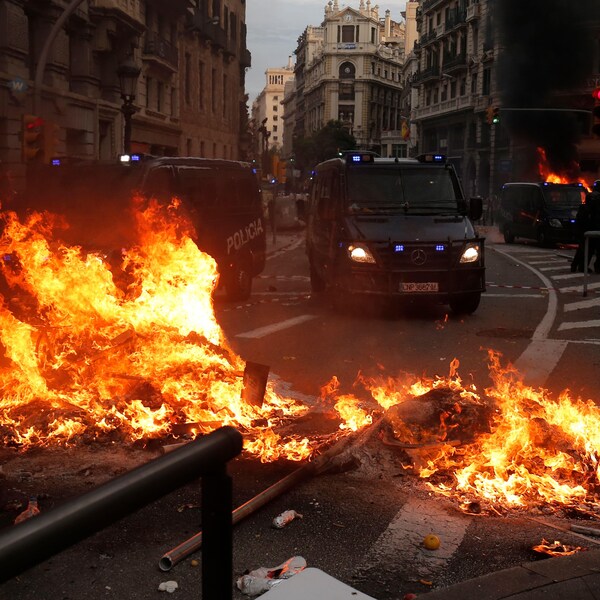 Des objets en feu au milieu d'une rue barrent le chemin aux camions de la police de Barcelone.