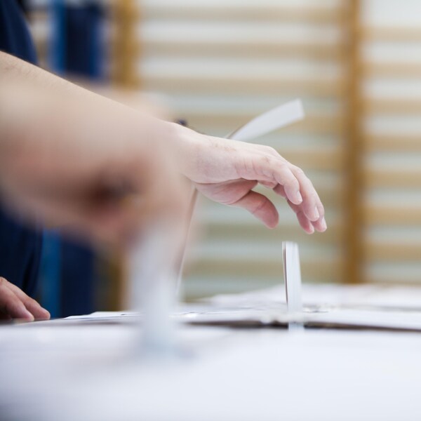 Une main dépose un bulletin de vote dans une urne.