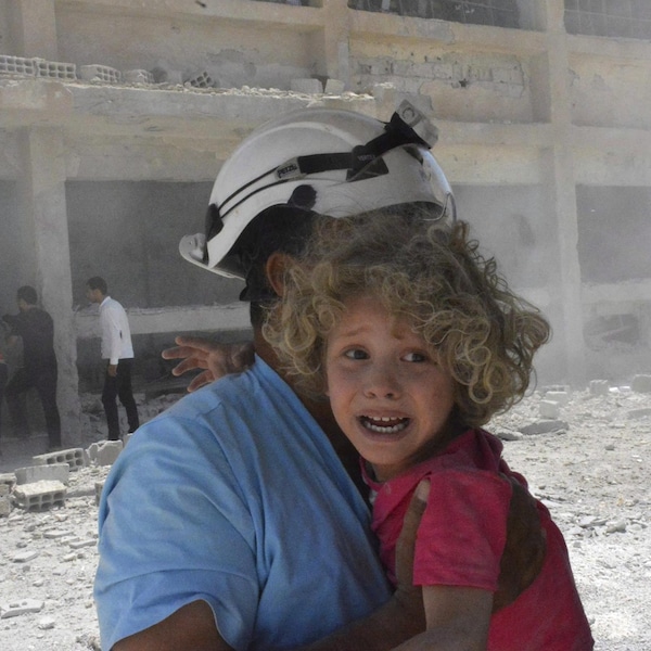 Une fillette pleure dans les bras d'un homme portant un casque blanc.