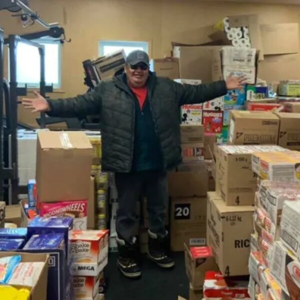 Un homme avec les bras étendus dans un entrepôt rempli de denrées.