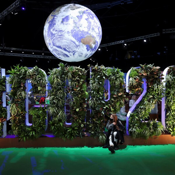 Une femme est assise devant une installation où les lettres du mot COP26 sont composés de plantes. Une représentation de la planète Terre flotte au-dessus des lettres.