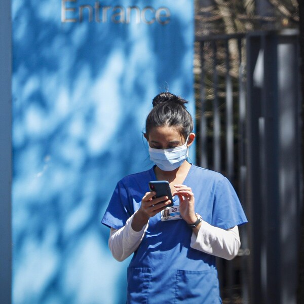 Une travailleuse de la santé portant un masque chirurgical consulte un message sur son téléphone intelligent.