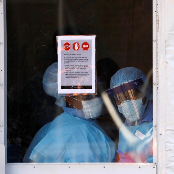Des infirmières en tenue de protection observent l’extérieur depuis une tente qui a été installée devant un centre hospitalier de New York. 