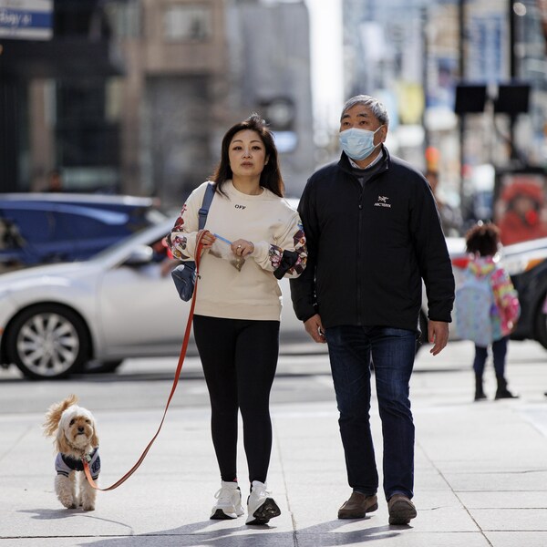 Un couple fait une promenade avec son chien dans une rue de Toronto. L'homme porte un masque sanitaire, mais pas son épouse.