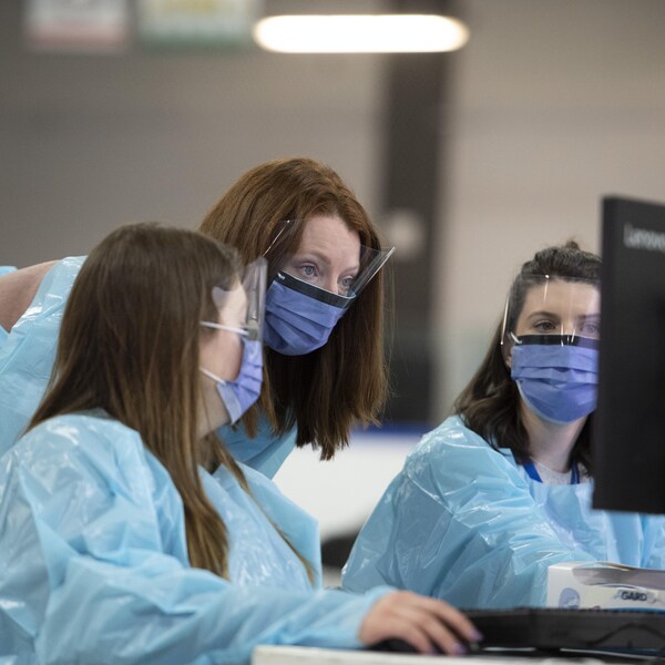 Trois travailleuses de la santé portant des masques regardent un écran d'ordinateur.