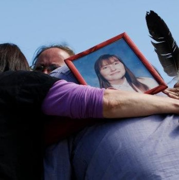 Quatre personnes se serrent dans les bras en portant la photo d'une femme.
