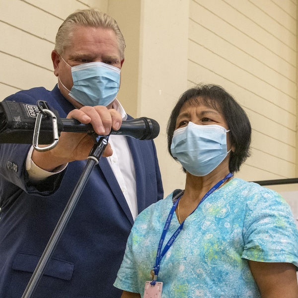 Le premier ministre de l'Ontario, Doug Ford, ajuste le microphone de la travailleuse de première ligne Anita Quidangen après qu'elle ait reçu la première dose du vaccin Pfizer-BioNTech à Toronto.