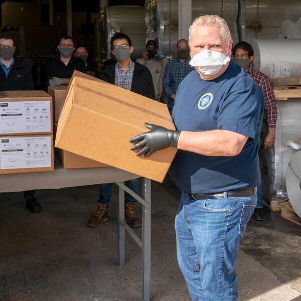 Doug Ford portant un masque et des gants tient une boîte en carton.