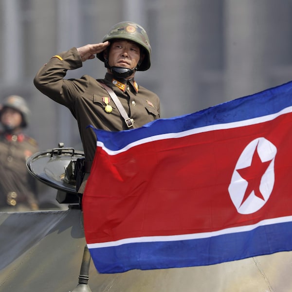 On voit un soldat dans un tank qui fait le salut militaire. Devant lui, le drapeau nord-coréen.