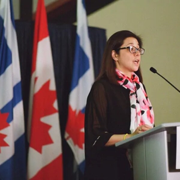 Elle parle à un lutrin devant des drapeaux du Canada et de Toronto.