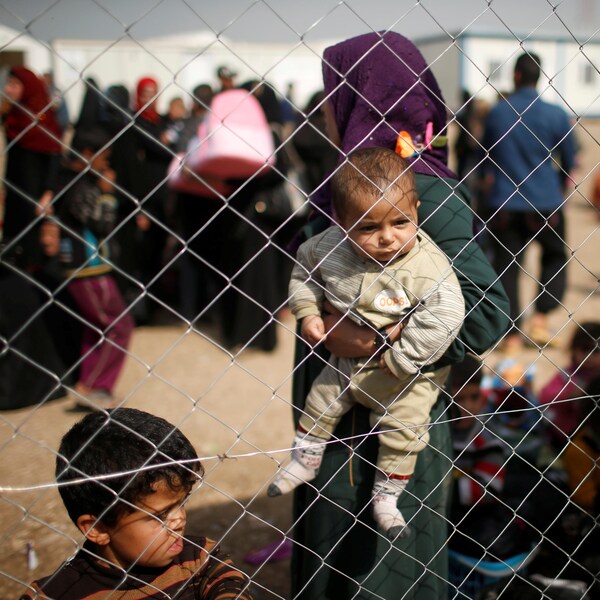 Des expatriés irakiens, photographiés derrière une clôture. Un enfant, dans les bras de sa mère, regarde la clôture.