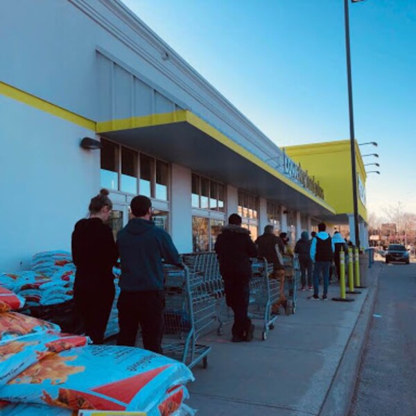 Des clients attendent en ligne avec leur panier à l'extérieur d'un supermarché.