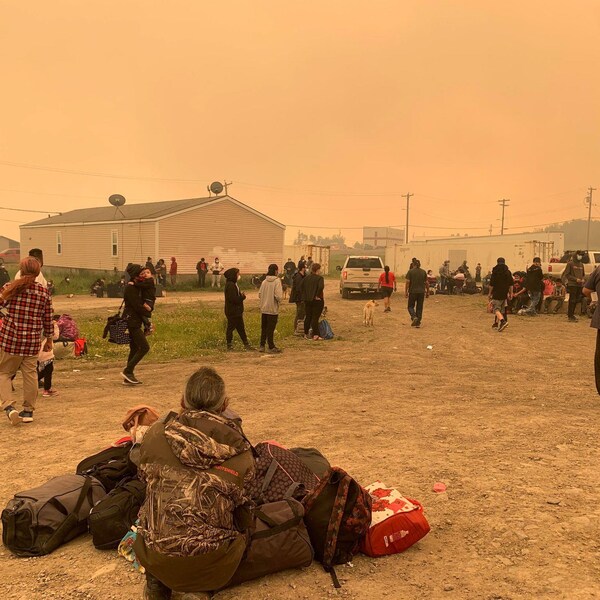 Des résidents réunis attendent: certains sont assis par terre entourés de valise, d'autres portent leur enfants dans les bras. 