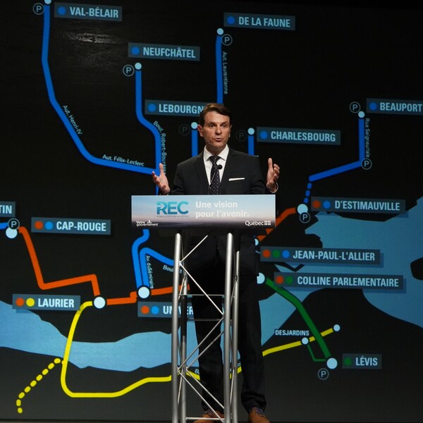 François Bonnardel derrière le podium lors de la conférence de presse avec la carte du Réseau express de la Capitale en arrière plan.