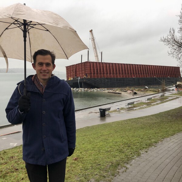 Gwendal Castellan, sous un parapluie, pose devant la barge échouée dans English Bay, à Vancouver.