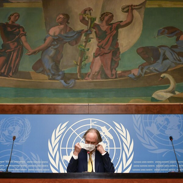 Un homme enlève son masque sur une tribune qui arbore le logo des nations unies et une énorme fresque.