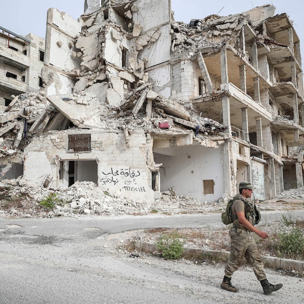Un soldat marche devant un immeuble en ruines.