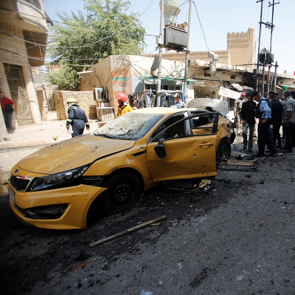 Des gens se rassemblent près d'une auto jaune canari qui est en partie démolie après qu'une explosion soit survenue.
