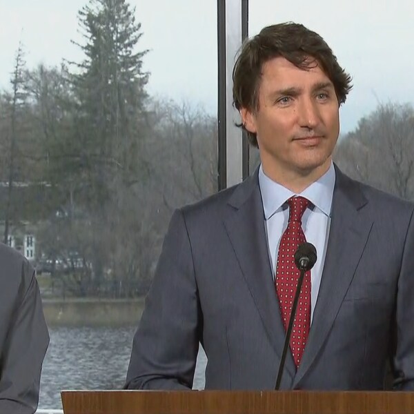 Justin Trudeau en point presse entouré de deux hommes.