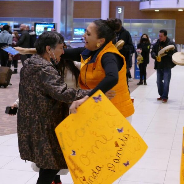 Deux femmes s'embrassent à l'aéroport international de Winnipeg, entourées d'autres personnes autochtones.  