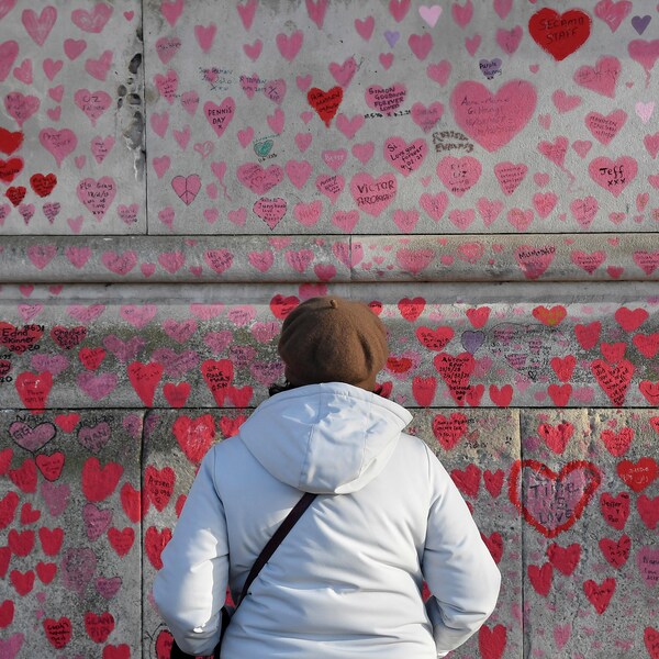 Une femme observe un mur de béton sur lequel sont peints des coeurs.