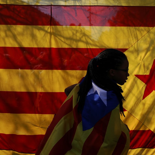 Une femme portant un drapeau indépendantiste catalan passe devant un autre drapeau coloré durant une manifestation à Barcelone. 