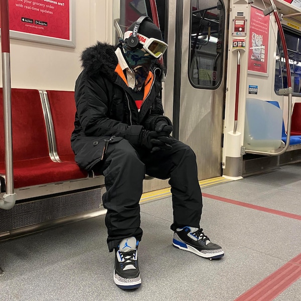 Un homme muni de lunettes de ski, d'une cagoule et de gants assis dans un wagon de métro.