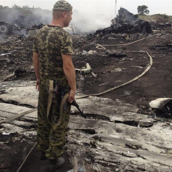 Un homme en treillis militaire et tenant une arme est debout au milieu de débris encore fumants.