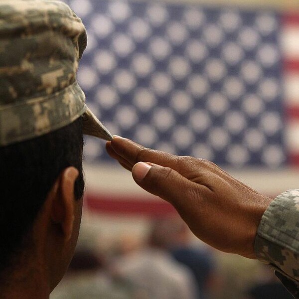 Un homme vêtu d'habits de l'armée fait le salut militaire devant un drapeau des États-Unis.