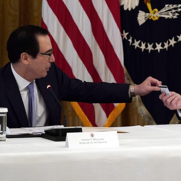 Donald Trump sourit à Steven Mnuchin, qui lui remet une carte de débit qui sera utilisée pour envoyer des paiements par le département du Trésor aux Américains lors d'une réunion de cabinet dans la salle Est de la Maison Blanche