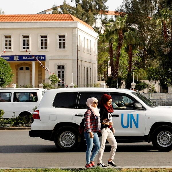 Deux jeunes femmes passent devant un véhicule blanc des Nations unies.
