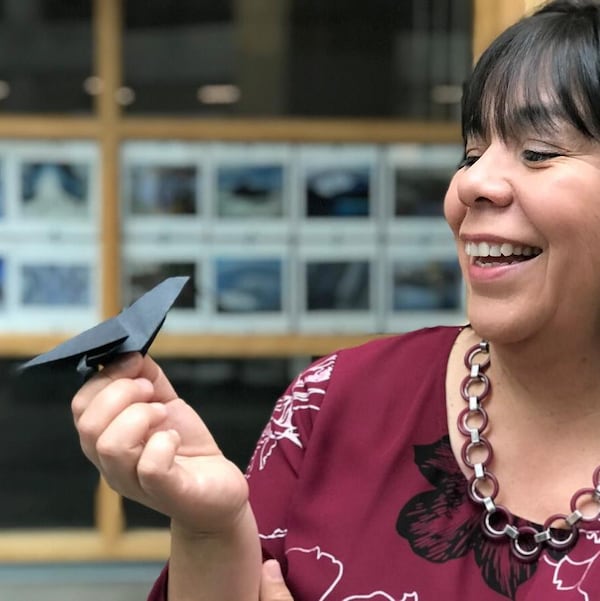 Une femme souriante tient un petit oiseau en origami fait de papier noir, représentant un corbeau.