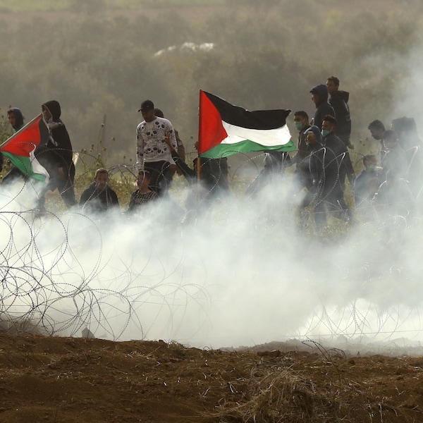 Des jeunes manifestants portant le drapeau palestinien au milieu d'une fumée de gaz lacrymogène, non loin de la frontière israélienne.