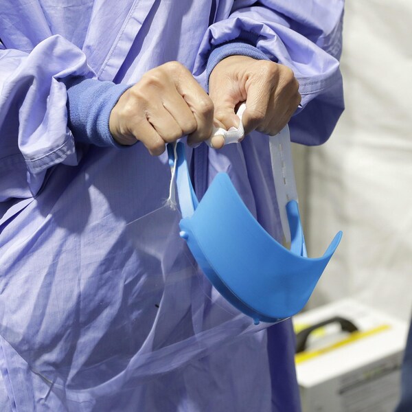 Une infirmière vêtue d'une jaquette médicale bleue ajuste une visière.