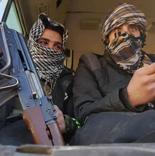 Deux rebelles évacués de la Ghouta sont assis côte-à-côte dans un autobus. L'un tient une arme, l'autre, un téléphone cellulaire.