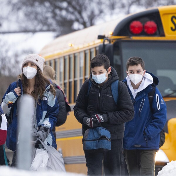 Des élèves portant un masque débarquent d'un autobus scolaire.