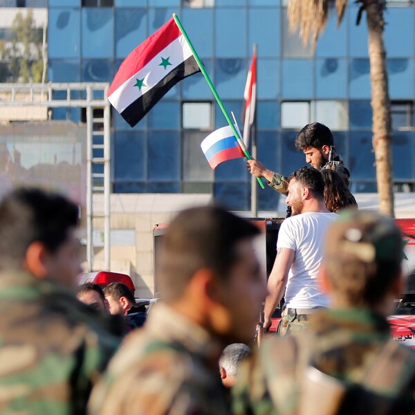 Un soldat syrien agite un drapeau russe ainsi qu'un drapeau syrien à Damas.