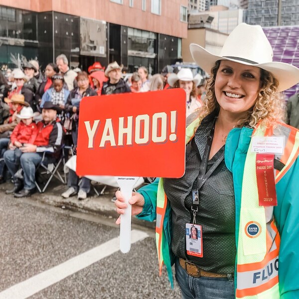 Devant une foule, une dame sourit à la caméra, portant un chapeau de cowboy et en tenant un ensigne qui est écrit YAHOO!