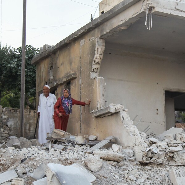 Un couple regarde les décombres d'une maison bombardée. 