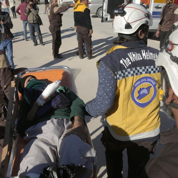 Des membres des Casques blancs (aussi appelés Défense civile syrienne) transportent un homme couché sur une civière, la main droite enroulé dans un bandage.