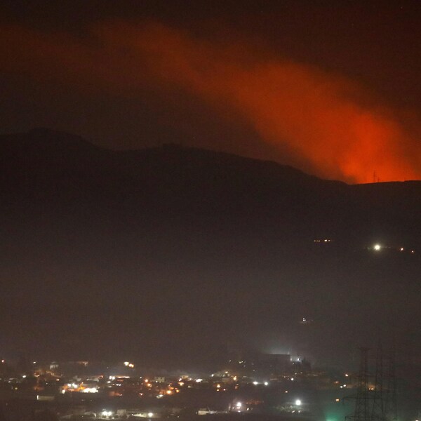 Une vue sur une colonne de fumée rougeâtre s'élevant derrière des montagnes dans la nuit près de Damas, en Syrie.
