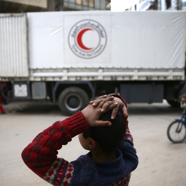 Un garçon se tient la tête devant un convoi humanitaire.