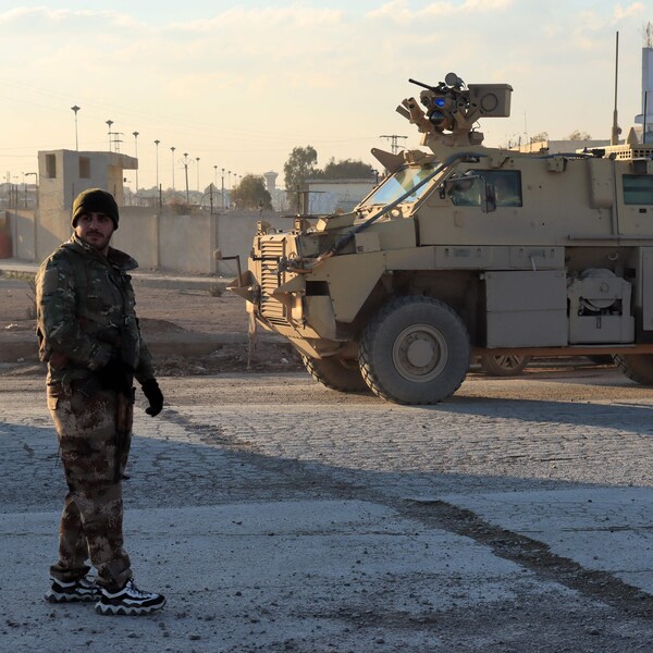 Un combattant en treillis militaire, près d'un véhicule blindé.