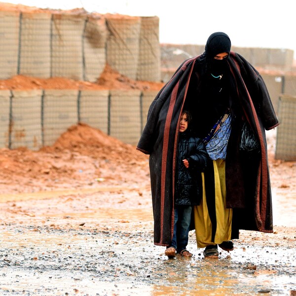 Une femme voilée, portant une une couverture sur les épaules et protégeant sa fillette de la pluie. 