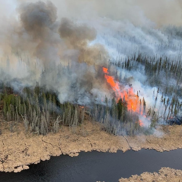 Feu de forêt avec fumée et flammes, près d'une rivière, le 15 mai 2023, à Hay River, aux Territoires du Nord-Ouest.