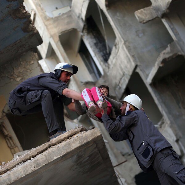 Trois hommes habillés de gris et portant des casques blancs secourent une petite fille habillée de rose des décombres, lors d'un exercice.
