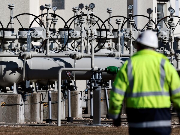 Un ouvrier marche près de valves et de toyaux à L'extérieur.