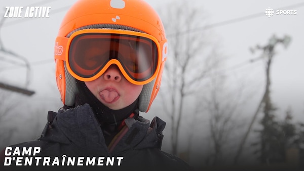 Un enfant avec un casque et des lunettes de ski tire la langue.
