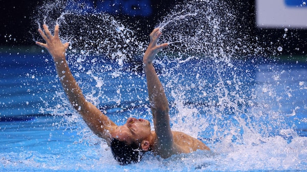 Un homme tend ses bras pendant une compétition de natation artistique dans une piscine.