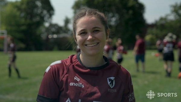 Une joueuse de rugby sourit sur un terrain.